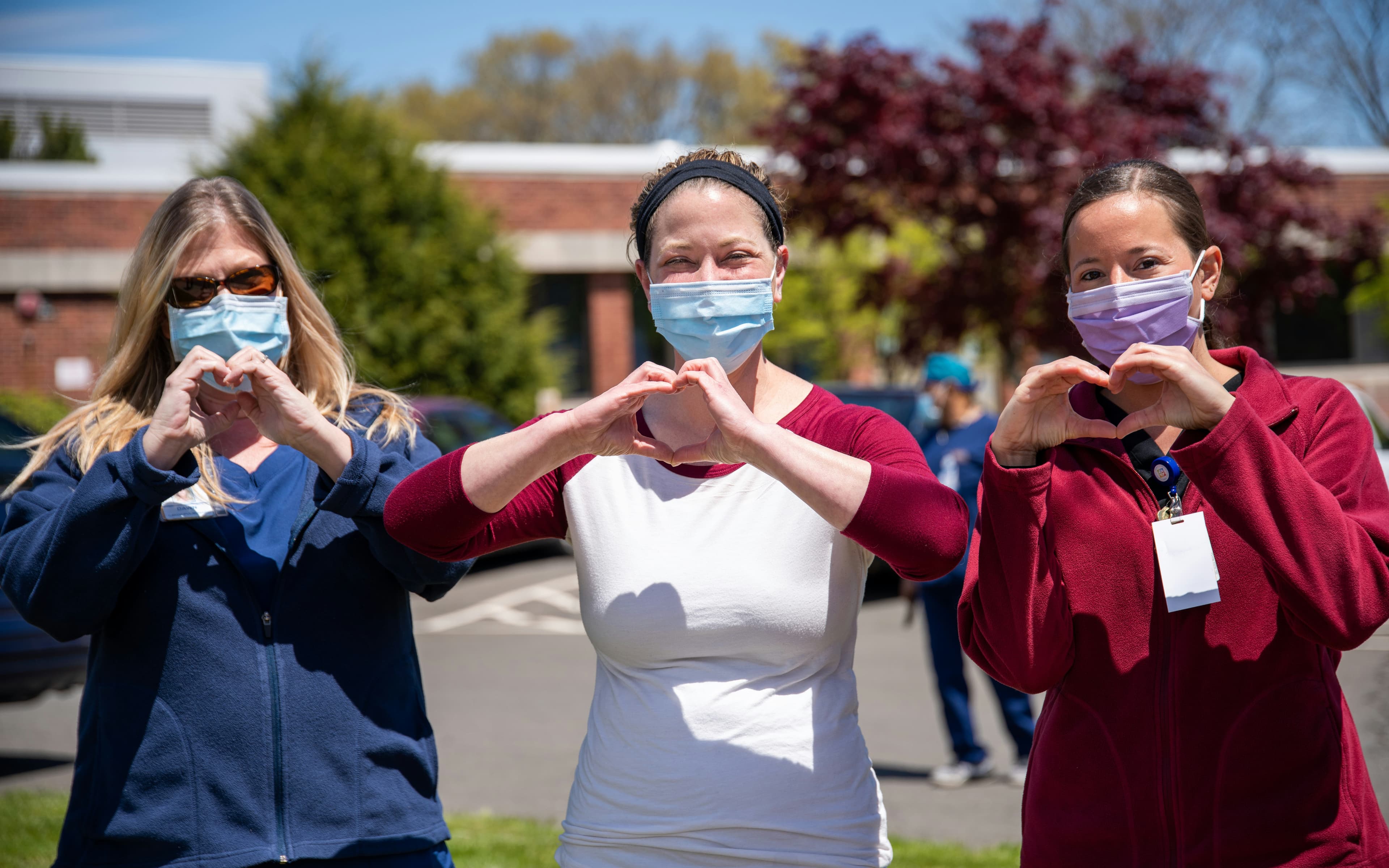 Three nurses outside making heart shapes with their hands