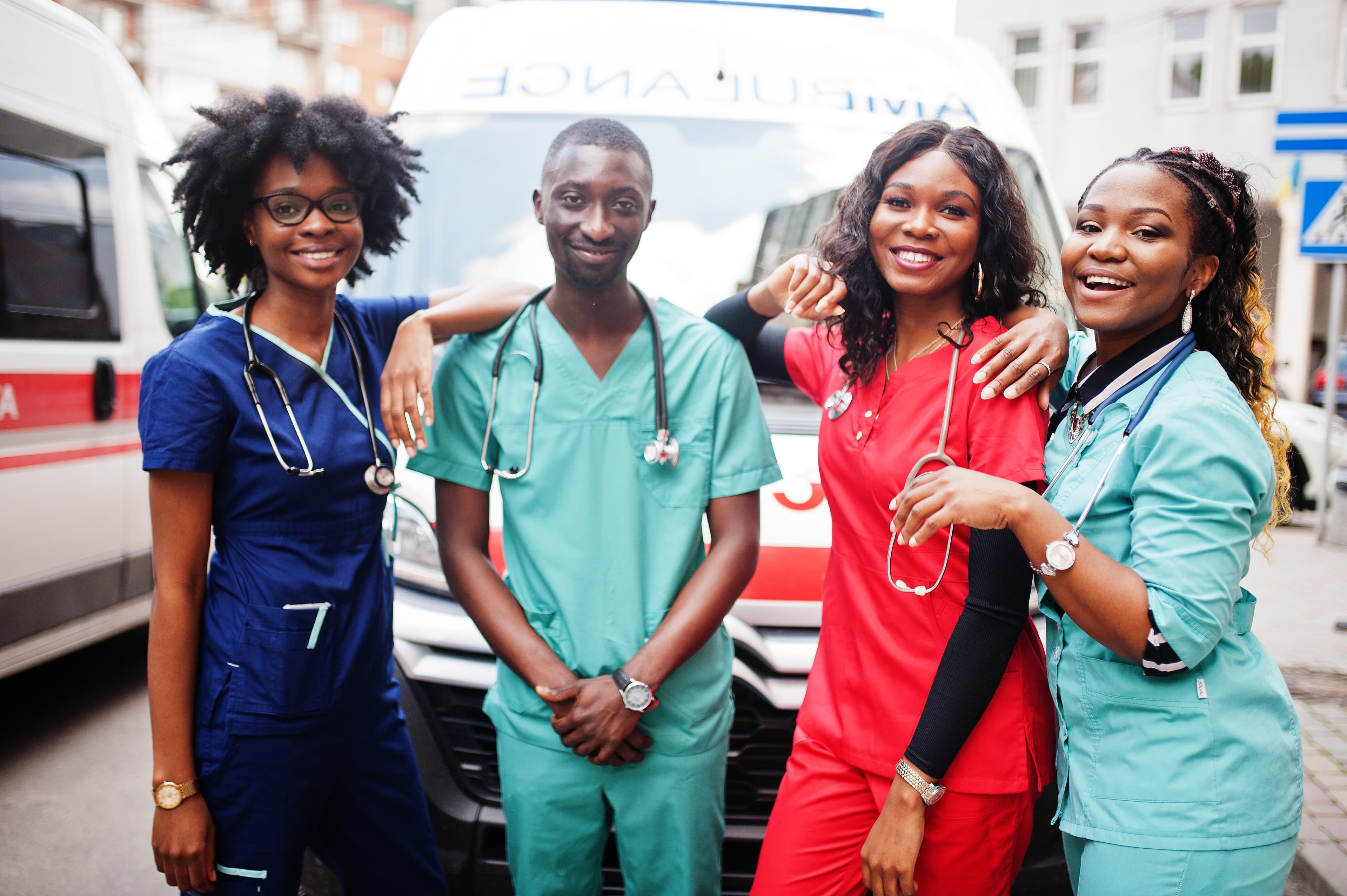 Group of four nurses smiling together in front of an ambulance