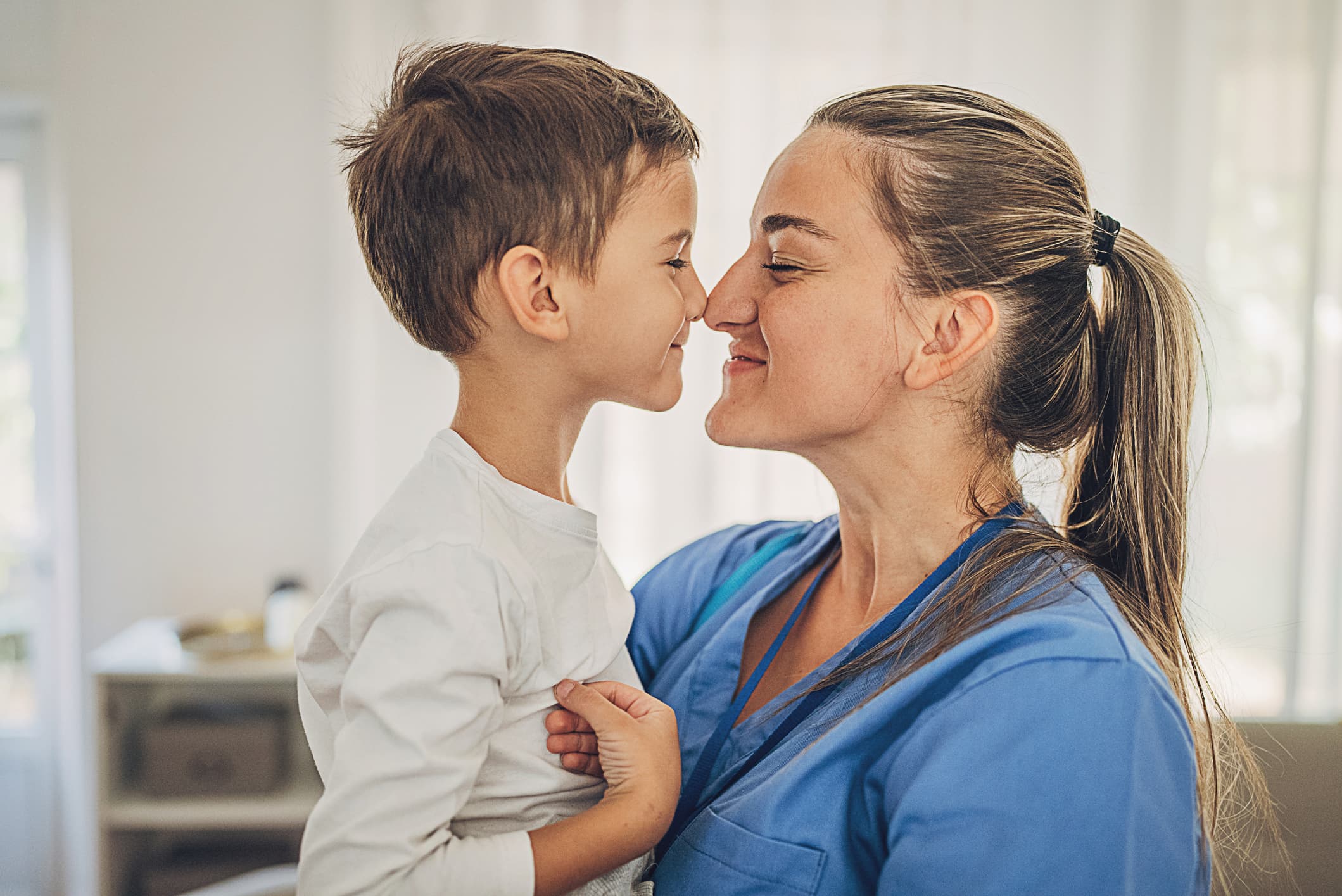 Nurse mom in blue scrubs touching noses with her son